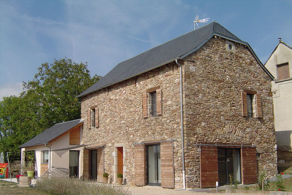 Ancienne grange en pierres rénovées avec petite extension en maçonnerie enduite et bardage bois. Menuiseries aluminiums et volets bois à lames horizontales, coulissants au RDC et battants à l'étage