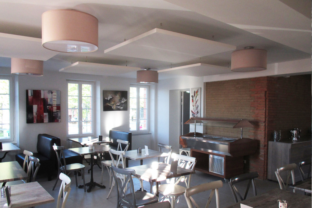 Aménagement de l'étage du restaurant avec baffles acoustiques en plafond et, visible au fond à droite, un mur en brique de terre crue existant conservé