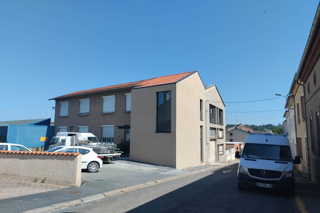 La surface de vente située à l'étage a nécessité la création d'une extension intégrant 2 escaliers et un élévateur vertical pour répondre aux normes PMR. Sa volumétrie répond côté rue au pignon existant et suit la géométrie de la toiture du bâtiment attenant. Plus spécifique, la grande ouverture amène depuis la rue le regard jusqu'à l'entrée de la nouvelle salle de vente.